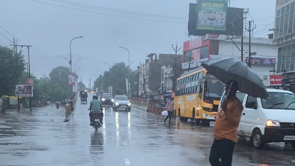 बांदा में बारिश के रेड अलर्ट में भारी बरसात में गुजरते लोग और वाहन।