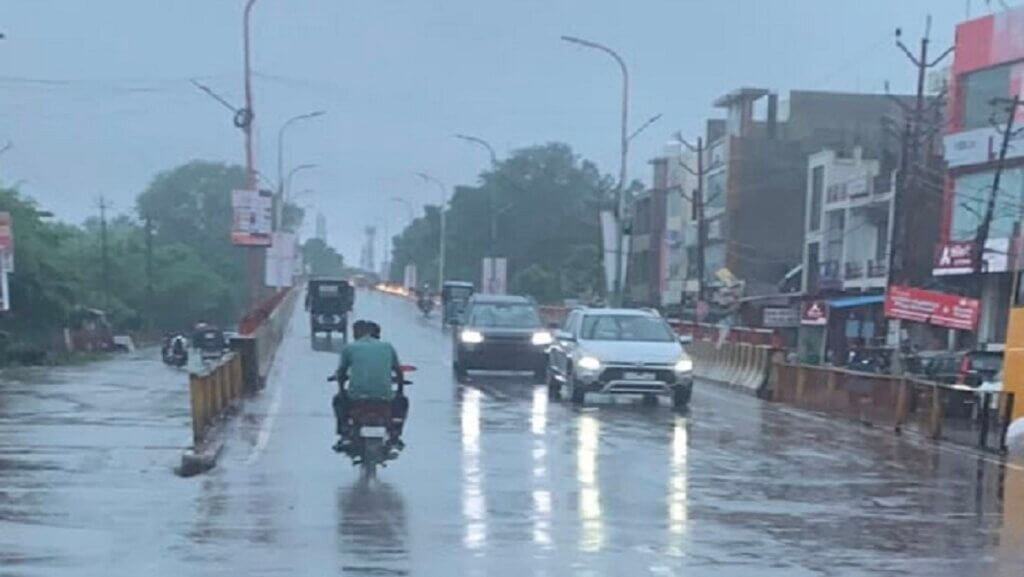 यूपी में 25 जिलों में भारी बारिश अलर्ट के बीच बरसात में गुजरते लोग